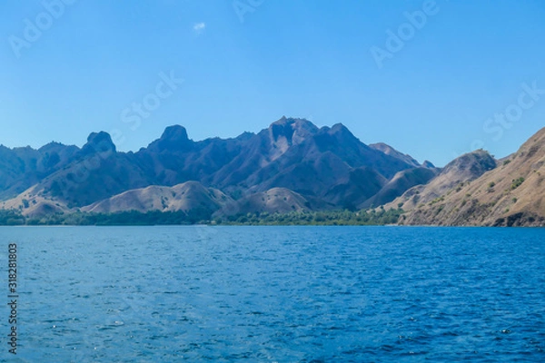 Fototapeta A view on idyllic island in Komodo National Park, Indonesia. There are few clouds above the island. Calm and clear surface of the sea. Island hoping. Perfect day for sailing