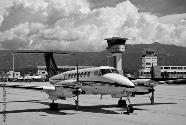 Obraz A private turboprop Beechcraft aircraft parked at Ajaccio airport on a black and white shot with stormy clouds and sky during a summer afternoon
