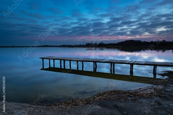 Fototapeta A long wooden bridge towards the water, evening blue and pink clouds after sunset in Staw, Poland