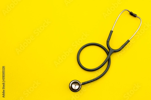 Obraz Above shot of a stethoscope puts on the left side of a table on a yellow background.