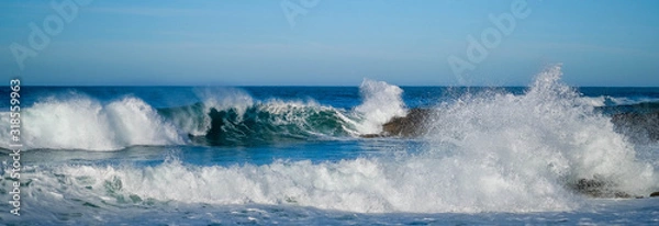 Fototapeta Large ocean waves crash against coastal stones on sunny day on European coast. Holidays, vacations on Atlantic ocean. High waves, surfing in Europe. Panoramic view. Tidal bore. Bay of Biscay, Spain.