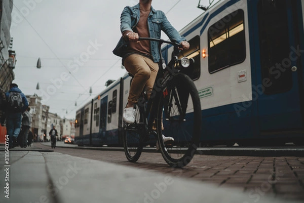 Obraz Netherlands, Amsterdam, 28 october, 2017: Young hipster guy driving modern black bicycle on cycle track, tram on the background