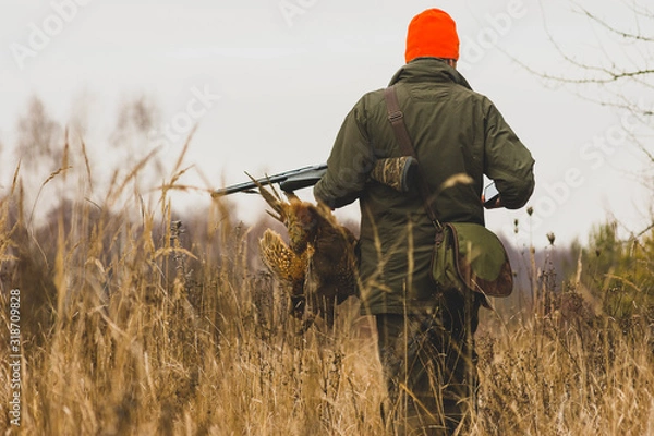 Fototapeta Hunter with prey, a pheasant in his hand at a field.