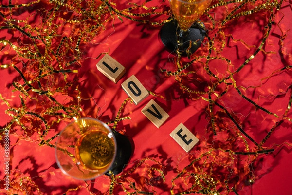Obraz Two sparkling champagne glasses, with gold confetti and red background with wooden pieces with the message love.