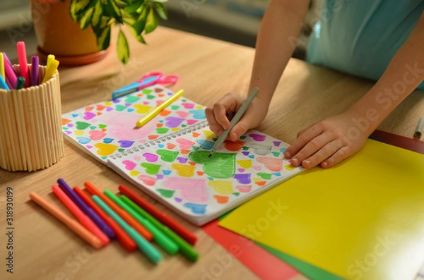 Fototapeta  Child's hands draw hearts of different colors in a notebook. Close-up photo.