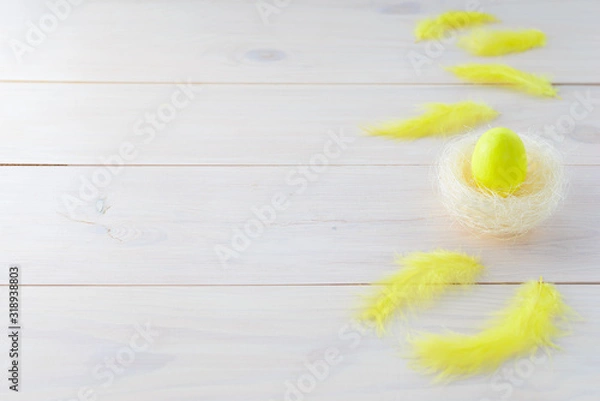 Fototapeta Easter egg in a nest with yellow feathers. Horizontal orientation, copy space.