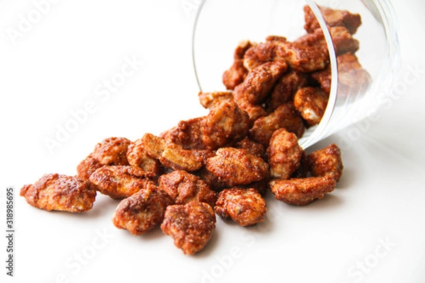 Fototapeta Sugar roasted pecan nuts (caramelized, praline nuts) in a glass on a white background, back view