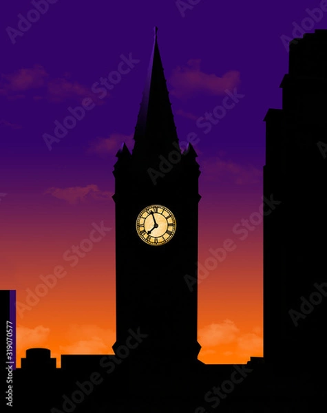 Fototapeta A clock tower is seen silhouetted at sunset with itâ€™s lighted clock face glowing in the dark.