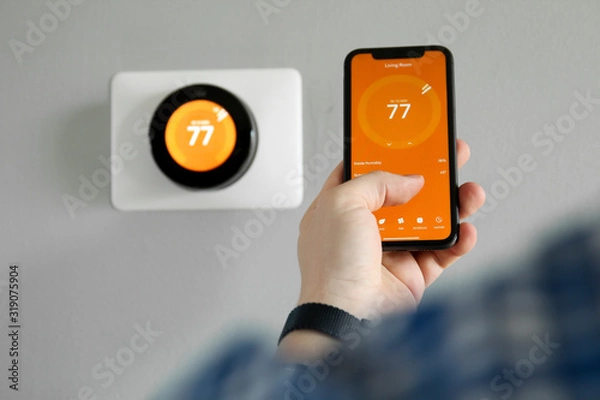 Fototapeta Man uses a mobile phone with smart home app in modern living room
