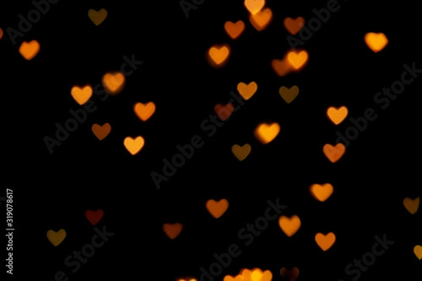 Fototapeta Black background with bright warm heart shaped bokeh lights. Holiday, Valentines Day background. Ideal to layer with any design. Horizontal