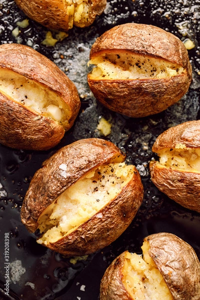 Obraz Baked potato, hot baked potatoes with the addition of butter and freshly ground black pepper and sea salt flakes on a black background, top view