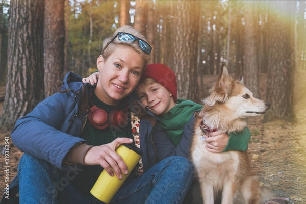 Obraz Charming little boy with a beautiful mother in headphones and a red dog on the autumn lawn