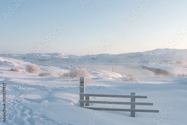 Fototapeta broken wooden fence in deep white snow on the outskirts of the village beyond the Arctic Circle on a frosty sunny day