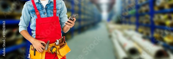 Fototapeta Smiling young man working in a warehouse standing with a bag of product over his shoulder grinning happily at the camera, close up view