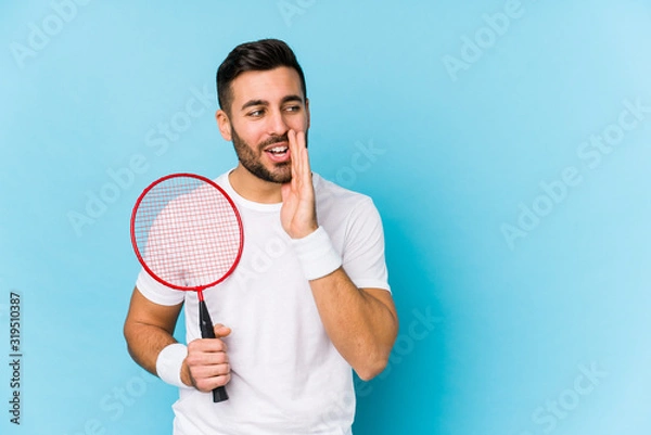 Fototapeta Young handsome man playing badminton isolated is saying a secret hot braking news and looking aside