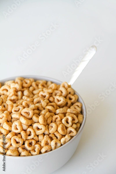 Fototapeta Bowl of whole grain oat cereal with a silver spoon on a white background , back view. Heart shapes cereal. 