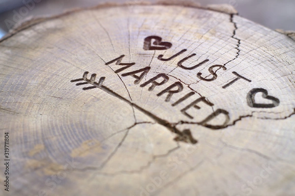 Fototapeta Just married. An inscription on a cut of a tree for a wedding decoration. Handmade decorative board on oak. Photo for your invitation design.
