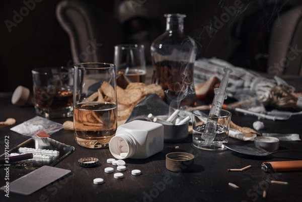 Fototapeta Various drugs, alcohol and cigarettes are on the wooden table. Substances that cause drug and alcohol dependence. Low key.