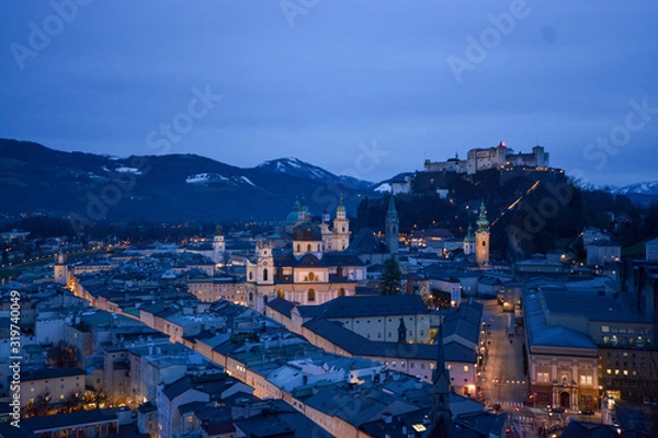 Fototapeta Salzburg evening cityscape with main Cathedral, Kollegienkirche and illuminated streets of old town on background of mountains in clouds