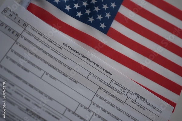 Fototapeta U.S. standard certificate of live birth application form next to flags of USA. Birthright citizenship concept. Diagonal view.