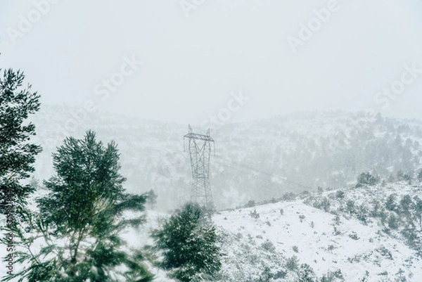 Fototapeta High voltage electric pole in the fog during a snow blizzard in the mountain.
