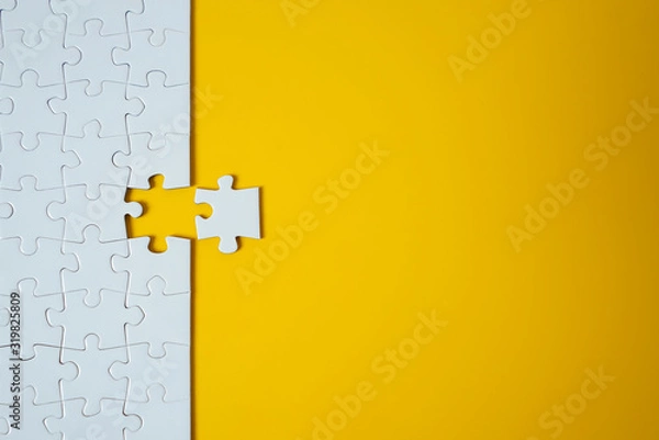 Fototapeta White jigsaw puzzle on yellow background. Team business success partnership or teamwork