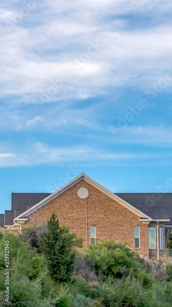 Fototapeta Vertical frame Blue sky and clouds over a home with gray roof and brick exterior wall