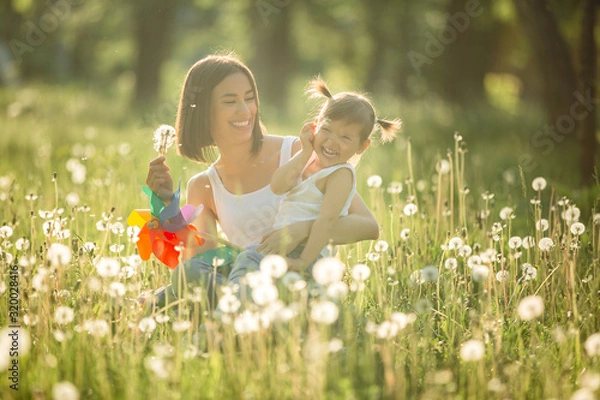 Obraz Portrait of happy mother and her little child on spring background. Cheerful family at dandelion field.Mom and her cute daughter outdoors.