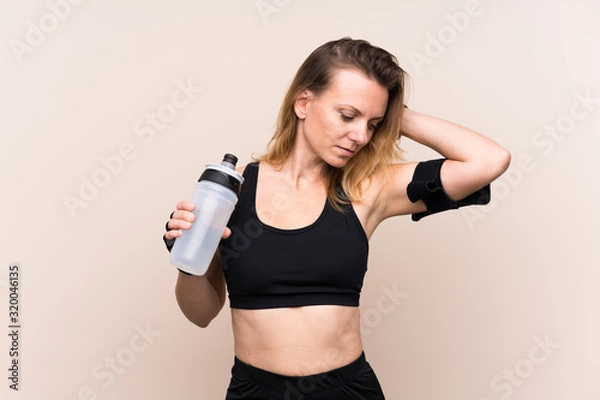 Fototapeta Blonde sport woman over isolated background with sports water bottle