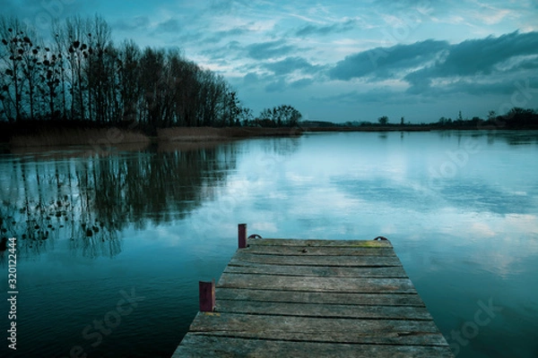Fototapeta Cloudy and cold winter evening, freezing lake with a pier