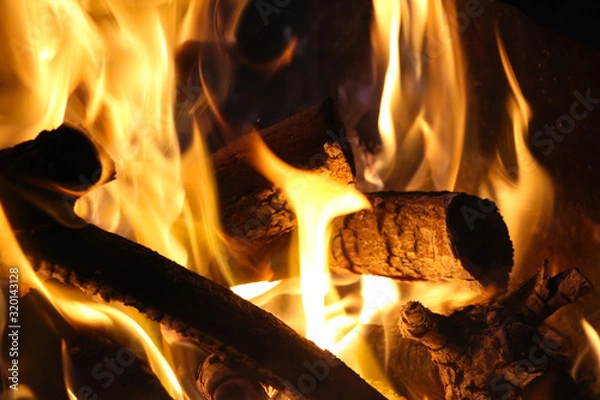 Fototapeta Close up view of orange flames in bonfire. Firewood is already charred. Theme of barbecue and outdoor recreation in a comfortable setting.