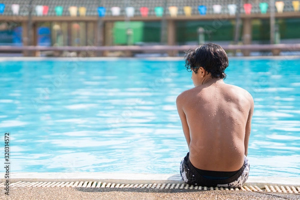 Fototapeta young boy sitting at the side of the swimming pool looking sad