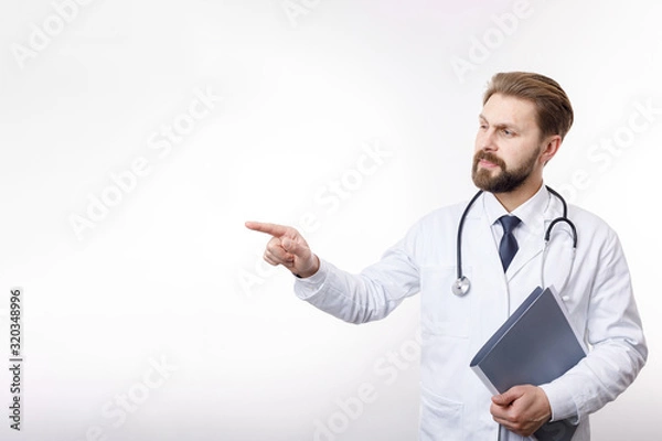 Fototapeta Intelligent physician in white smock and shirt pointing at something isolated white background copyspace