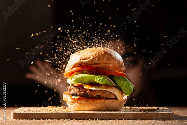 Obraz home made hamburger made by white sesame bun, tomato slice, salad, cheese, grilled meat and onion on wooden tray wooden table with cooking decorate chef hand in dark isolate background stock photo