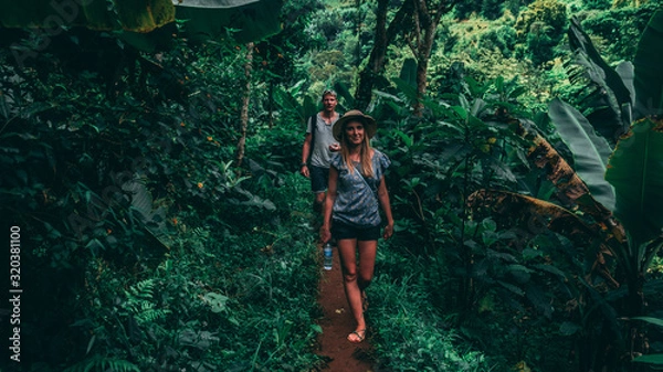 Fototapeta couple walking in a green jungle. Women with a hat, men with a backpack in Tanzania Africa
