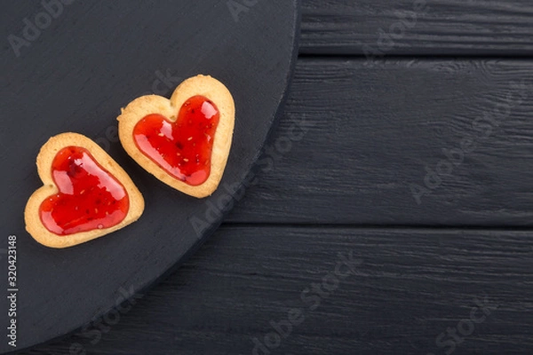 Obraz Heart shaped cookies decorated for Valentine's Day. Free space for text. Two heart shaped cookies with jam on a black wooden table. Like postcard 