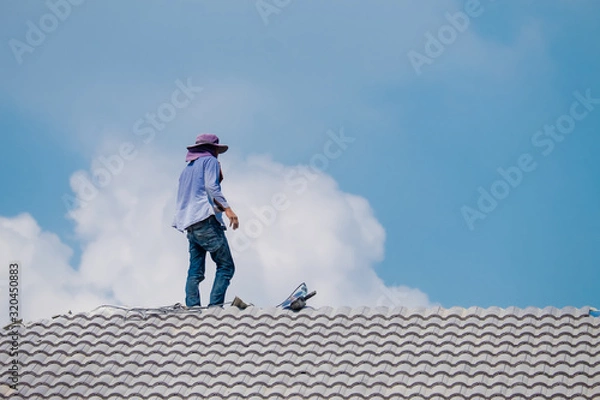 Fototapeta Workers installing gray concrete tiles on the roof with electric drill in house construction site.