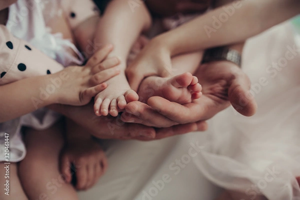 Fototapeta a family of three people without a face with light skin firmly hold the baby's small legs in their hands, a tender photo about a close family connection and family values