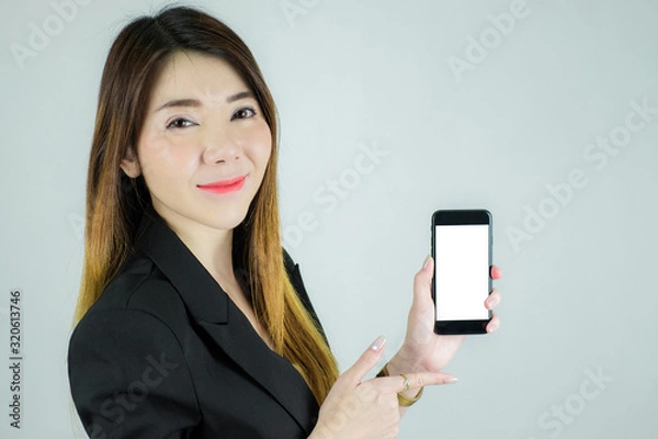 Obraz Portrait of stressed asian business woman showing and pointing to empty white mobile screen. Caucasian female model isolated on white background. selective focus