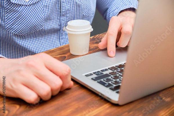 Obraz A man works behind a laptop on a wooden table with an hour of espresso.