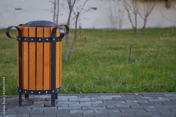 Obraz copy space on the left. Rubbish box in the park . A wooden urn and a comfortable empty park bench . Yellow garbage bin inside a wooden enclosure at a park.