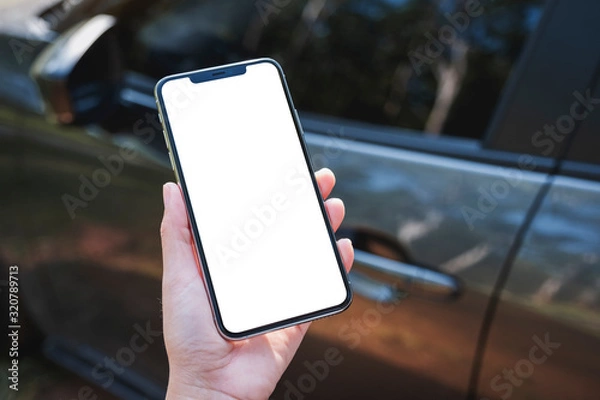Fototapeta Mockup image of a woman holding and using mobile phone with blank screen with a car in background