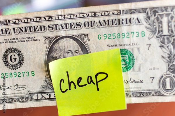Obraz Yellow stick note on an USD one dollar money background. The inscription "cheap" on a yellow memory sticky note. Close up