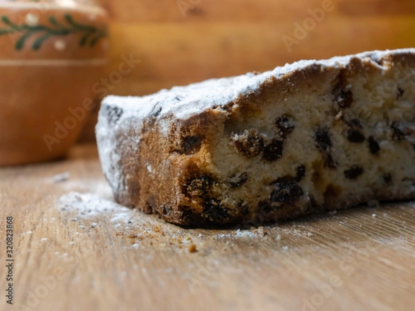Fototapeta Tasty, delicious pie with raisins, sprinkled with icing sugar, cut on a wooden table. Cupcakes for holidays, dough products. With clay vintage pot in the background