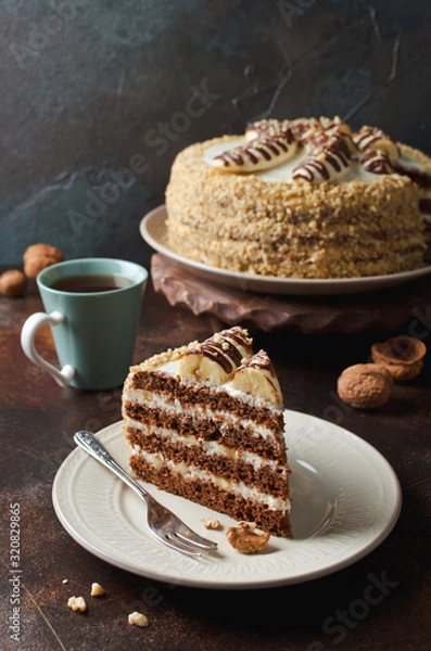 Fototapeta Chocolate cake with bananas decorated with chocolate topping and walnuts.