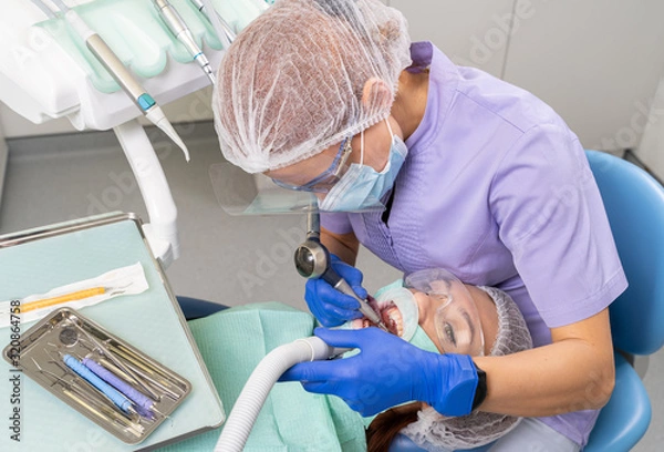 Fototapeta The dentist using specialized tools treats caries in the patient’s oral cavity using new technologies in dentistry.