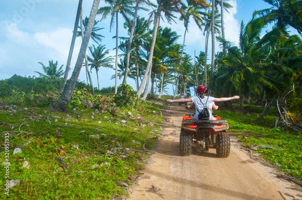 Fototapeta A group of people have fun on safari on quad bikes through the coconut beach near the shore