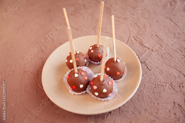 Fototapeta Chocolate candies covered with pink and red hearts on a stick lie on a white plate