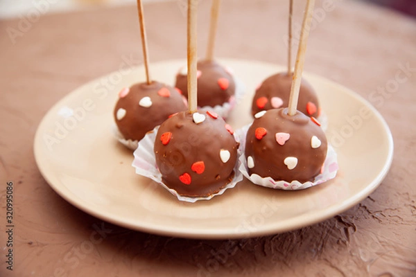 Fototapeta Chocolate candies covered with pink and red hearts on a stick lie on a white plate