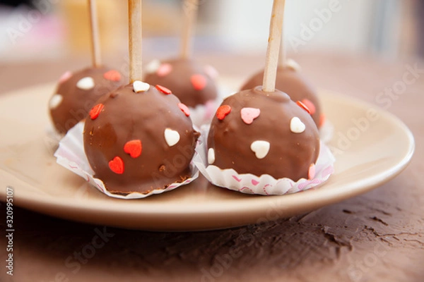 Fototapeta Chocolate candies covered with pink and red hearts on a stick lie on a white plate